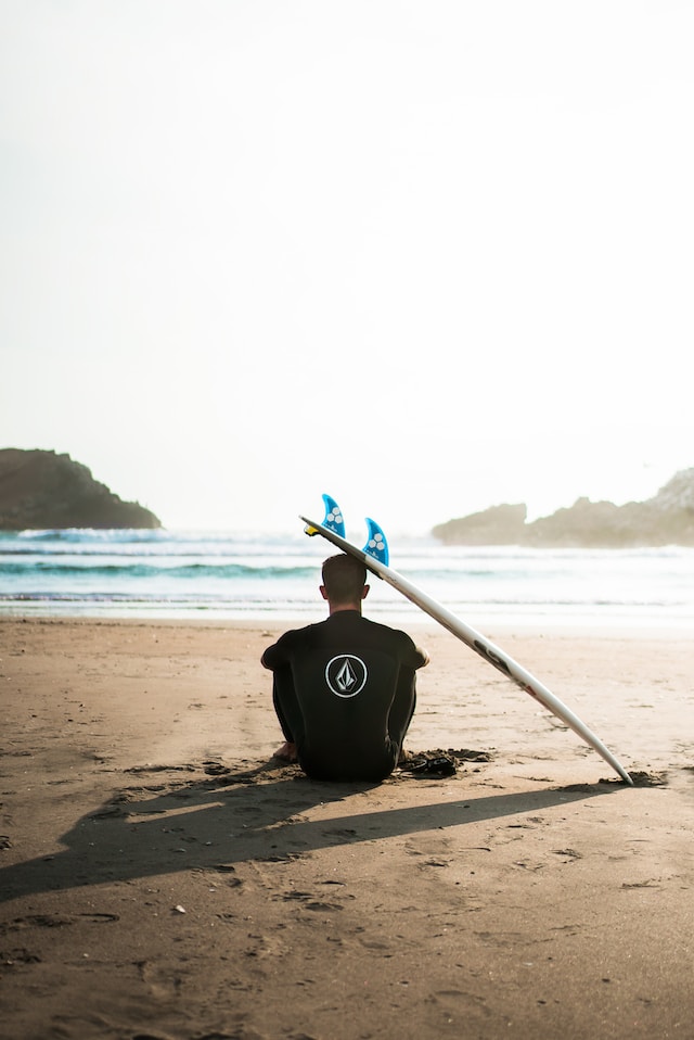 man balancing a surf board on his head on the beach